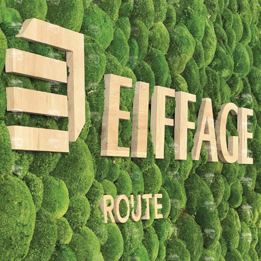 Logo d'Eiffage Route en lettres dorées sur un fond de mousse verte.