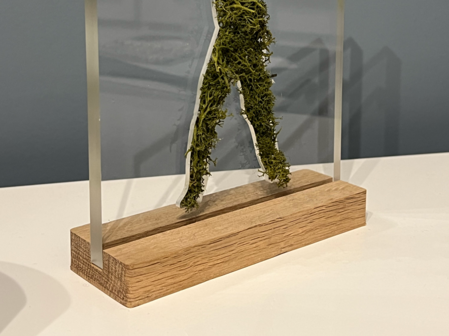 Sculpture d'une silhouette humaine en mousse verte sur socle en bois.