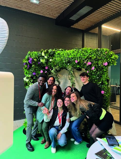 Groupe de personnes souriantes devant un mur de fleurs et de feuillage.