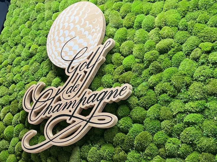 Logo "Golf & Champagne" sur un fond de mousse verte.