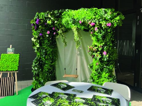 Arche décoratif végétal avec rideau, table et brochures sur une surface verte.