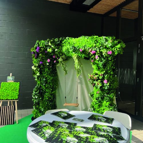 Arcade de verdure avec fleurs, table ronde et brochures sur une moquette verte.