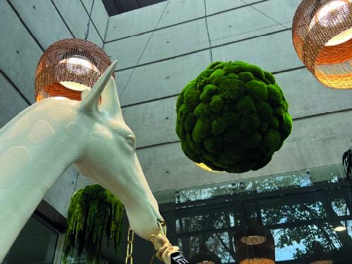 Tête de cheval blanc et boule verte de mousse sous des luminaires suspendus.