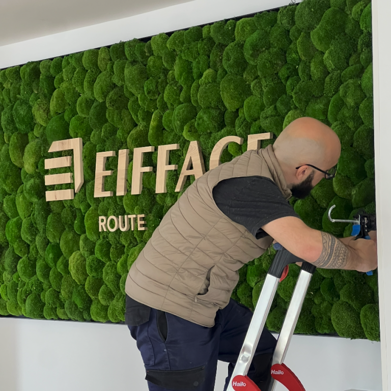 Un homme travaille sur un mur végétal avec le logo "Eiffage" en arrière-plan.