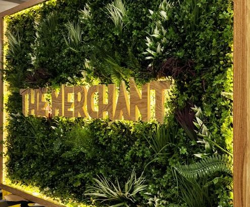Mur végétal avec le texte "THE MERCHANT" en lettres dorées.