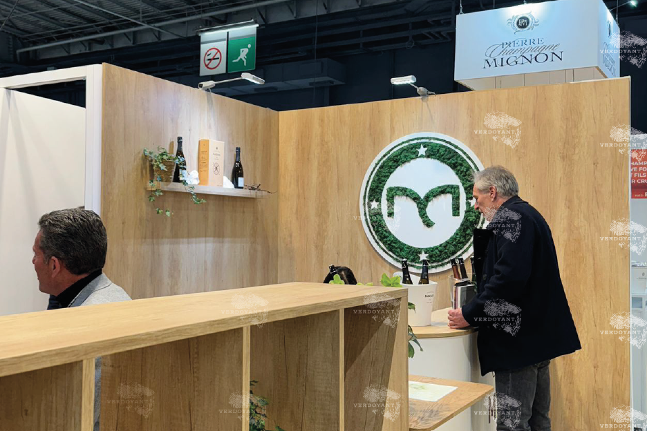 Stand d'exposition en bois avec un logo et des personnes discutant à l'arrière-plan.